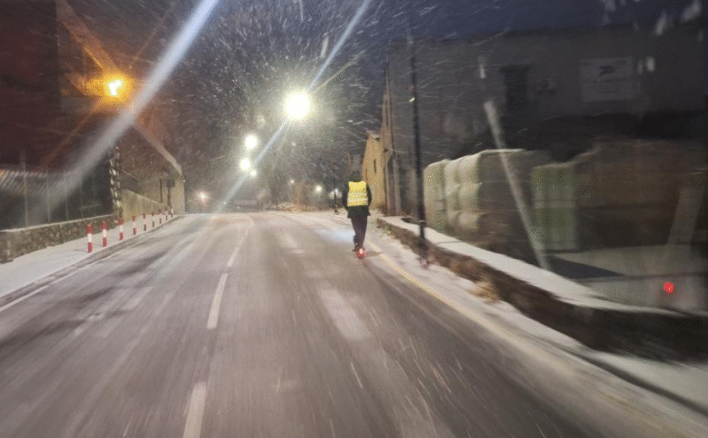 Un jove circulant per una carretera d'Andorra amb patinet elèctric mentre neva de nit.