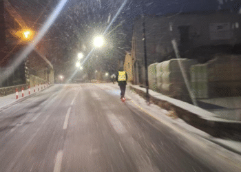 Un jove circulant per una carretera d'Andorra amb patinet elèctric mentre neva de nit.